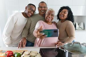Happy Latin family having fun taking selfie with mobile smartphone while preparing healthy lunch in modern kitchen at home - Food and parents concept photo