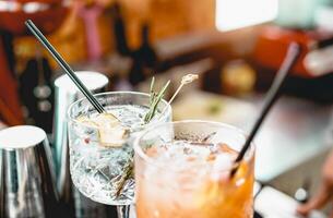 Cocktails served on bar counter prepared with gin, rosemary, paper and orange juice. Drink, nightlife, lifestyle concept. Focus on top crystal glass photo