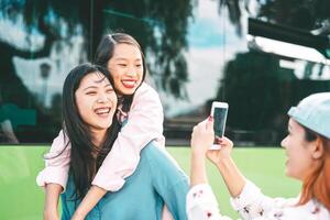 milenario asiático muchachas utilizando móvil teléfono al aire libre - joven contento personas teniendo divertido con nuevo teléfono inteligente aplicación tecnología fuera de - concepto de amistad, tecnología y juventud adolescente estilo de vida foto