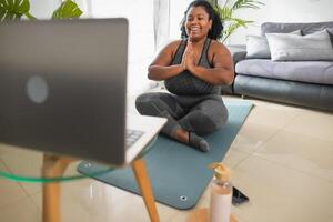 africano joven mujer haciendo yoga virtual aptitud clase con ordenador portátil a hogar - e-learning y personas bienestar estilo de vida concepto foto