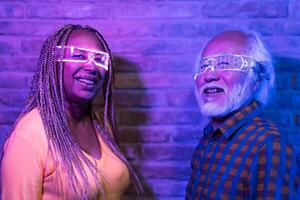 Happy senior friends having fun with futuristic augmented reality glasses - Metaverse concept photo