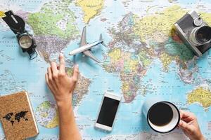 Top view of young woman planning her vacation using world map while drinking coffee - Tourist pointing the next travel destination - Concept of adventure, tourism, and traveling people lifestyle photo