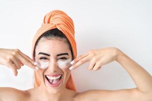 Happy girl applying daily facial cream - Young woman having skin care spa day - Beauty clean treatment and cosmetology products concept photo