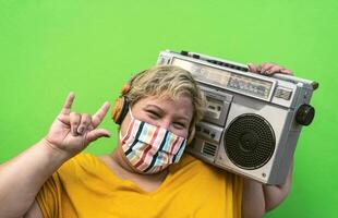 Plus size woman listening to music with wireless headphones while wearing face protective mask to avoid corona virus infection - Overweight people and health care concept photo