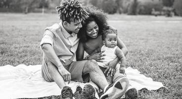 Happy African family having fun during the weekend in public park - Mother and father playing with their daughter outdoor - Love, parenthood and happiness concept - Black and white edited photo