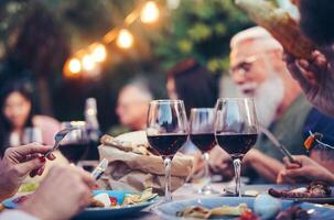 contento familia comiendo y Bebiendo rojo vino a cena parilla fiesta al aire libre - maduro y joven personas comida juntos en techo - juventud y mayor fin de semana estilo de vida ocupaciones - atención en Copa de vino foto