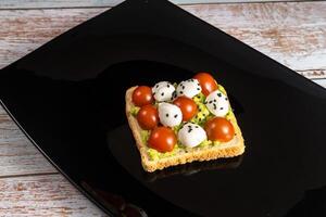 A cheese and tomato sandwich sits in a black plate on a wooden background photo