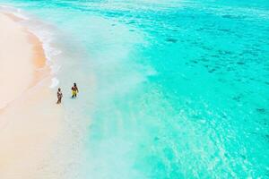 An aerial view of a couple standing on a tropical beach with a view of breaking waves on a tropical Golden sand beach. Sea waves gently loop along the beautiful sandy beach photo