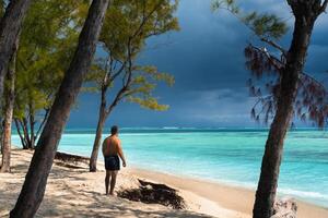A beautiful relaxed young man in black shorts stands on the beach of the island of Mauritius photo