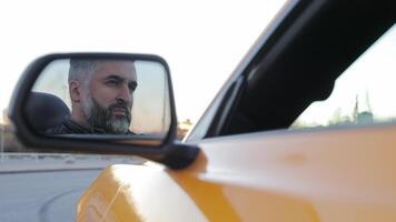 canto del hombre reflexión en coche espejo, de cerca reflexión de un hombre apasionadamente canto en el lado espejo de un amarillo convertible coche. video