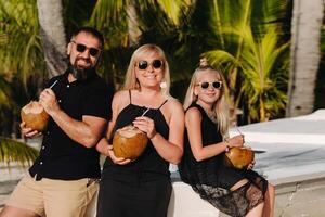 un elegante familia en negro ropa con cocos en su manos en el playa de el isla de mauricio.hermoso familia en el isla de Mauricio en el indio Oceano foto