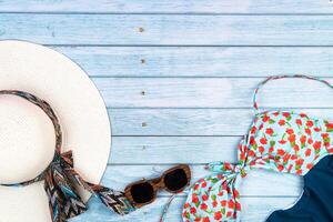 Top view of a straw white hat with glasses and a swimsuit, lying on a blue wooden background.Summer vacation concept photo