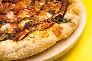 Delicious large pizza with bacon and spinach on a yellow background photo