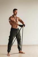 A man with a naked torso is engaged in strength fitness using a rubber loop indoors photo