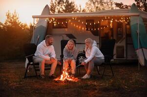 A family cooks sausages on a bonfire near their motorhome in the woods photo