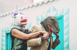 loco mayor Pareja vistiendo unicornio y tirano saurio Rex máscara mientras bailando al aire libre - maduro de moda personas teniendo divertido celebrando carnaval hora - absurdo concepto de mascarada gracioso Días festivos foto