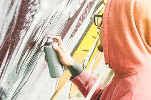 Street artist painting graffiti with color spray his art on the wall  - Young man writing and drawing murales on the street - Urban lifestyle and contemporary art concept photo