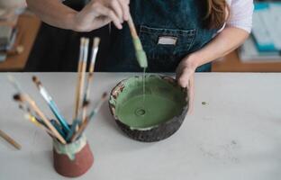 Woman mixing paint with brush inside ceramic bowl in workshop studio - Artisan work and creative craft concept photo