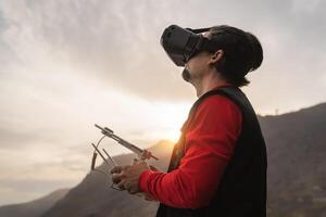 Male professional drone pilot doing fpv experience with virtual reality glasses during sunset time - Technology and innovation concept photo