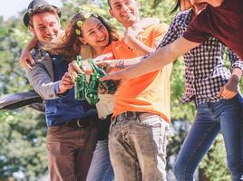 grupo de amigos aplausos y Bebiendo cervezas al aire libre - contento joven personas teniendo divertido tostado botellas de cerveza y riendo juntos - amistad, fiesta y juventud estilo de vida concepto foto