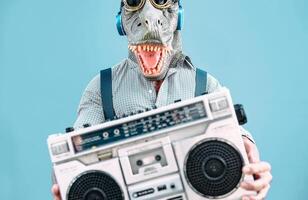 Crazy senior man wearing t-rex mask and listening to music holding vintage boombox stereo outdoor - Fashion masquerade male having fun dancing and celebrating outside - Absurd and funny people concept photo