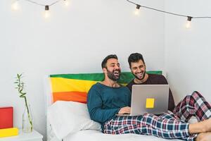 Happy gay men couple using laptop in bed- Homosexual love and gender equality in relationship concept photo