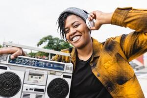 Happy African girl having fun listening to music with headphones and vintage boombox stereo photo