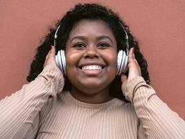 Happy Afro Latin girl having fun listening music with wireless headphones outdoor photo