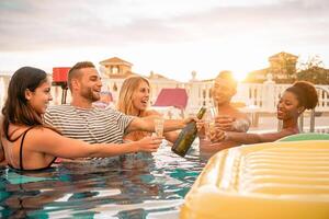 Happy friends toasting champagne at pool party  - Young people having fun drinking sparkling wine in luxury tropical resort at sunset - Summer holidays and vacation youth lifestyle concept photo