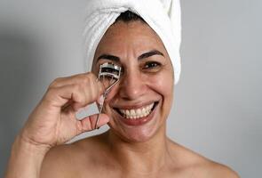 Happy Latin mature woman using eyelash curler - People beauty and wellness lifestyle concept photo