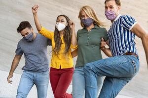 Young friends dancing together while wearing face mask outdoor - Happy people having fun in city after corona virus quarantine - Youth millennial generation friendship and health care concept photo