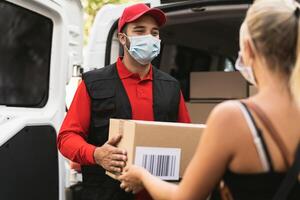 Delivery man wearing face protective mask to avoid corona virus spread - Young woman receiving an online order package from courier express photo