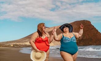 Happy plus size women having fun walking on the beach during summer vacations - Overweight people concept photo