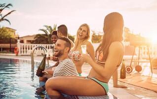 grupo de contento amigos haciendo un piscina fiesta a puesta de sol - joven personas riendo y teniendo divertido Bebiendo champán en vacaciones - amistad, vacaciones, juventud estilo de vida concepto foto