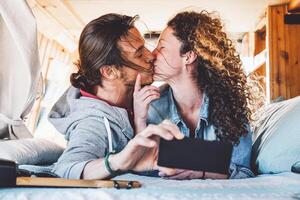 Happy couple kissing in vintage mini van during their roadtrip - Young romantic lovers having tender moments while taking photo with mobile smartphone camera - Travel, love and relationship concept