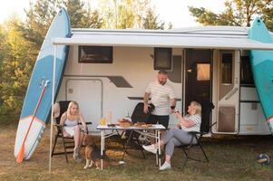 un contento familia es descansando cerca cerca su casa rodante en el bosque foto