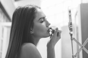 Beautiful young woman putting her lipstick on before going out for a night in town - Stunning girl applying makeup on and getting ready to go out in the club - Black and white vintage editing photo