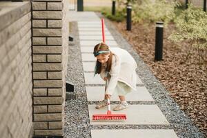 A little girl with a brush cleans a path on the street in the courtyard photo