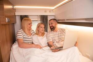 A family of three is watching a movie on a laptop while sitting in the bed of their motorhome photo