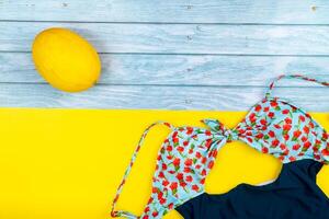 Top view of a swimsuit and a melon lying on a blue wooden and yellow background.Summer vacation concept photo