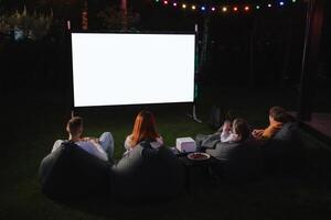 familia madre, padre y niños reloj un proyector, películas con palomitas de maiz en el noche en el patio foto