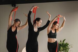 Girls in black are doing fitness with red ribbons indoors photo