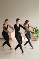 un grupo de muchachas en negro haciendo yoga poses adentro. mujer son comprometido en aptitud foto