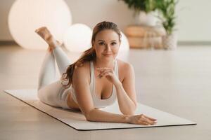 Portrait of a girl in white clothes lying on a mat before doing yoga indoors photo