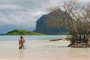 A girl in a swimsuit and a man in shorts stand in the ocean against the backdrop of mount Le Morne on the island of Mauritius.A couple in the water look into the distance of the ocean photo