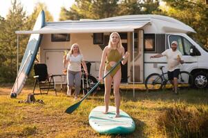 the family is resting next to their mobile home. My daughter is standing with a paddle on a sup board, and her parents pour water on her photo