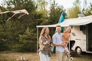 Happy parents with their child play with a kite near their motorhome in the forest photo