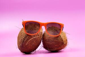 Two whole coconuts and orange glasses on a pink background. photo