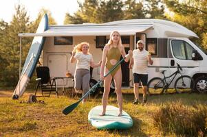 the family is resting next to their mobile home. My daughter is standing with a paddle on a sup board, and her parents pour water on her photo