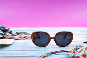 Top view of a straw white hat with glasses and a swimsuit, lying on a blue wooden background.Summer vacation concept photo